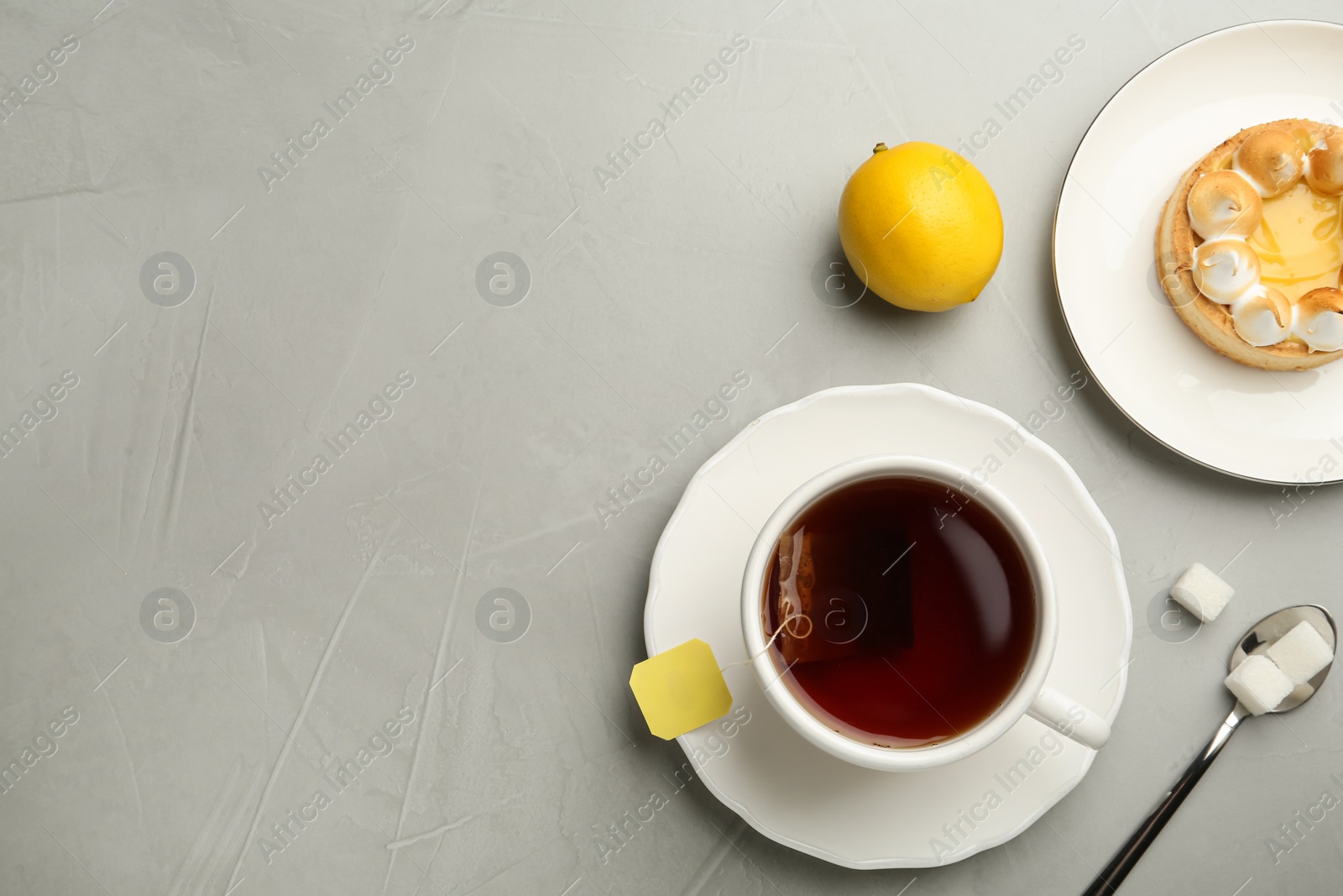 Photo of Flat lay composition with tea bag in ceramic cup of hot water and dessert on grey table. Space for text