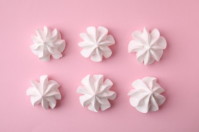 Many tasty meringue cookies on pink background, flat lay