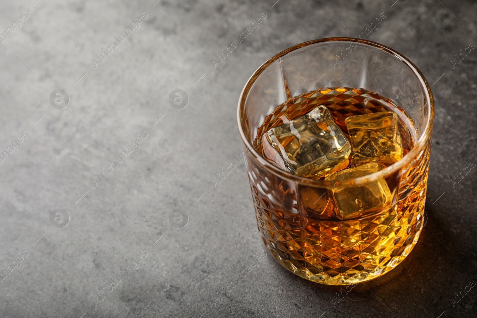 Photo of Golden whiskey in glass with ice cubes on table. Space for text