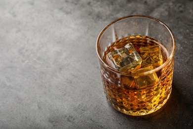 Photo of Golden whiskey in glass with ice cubes on table. Space for text