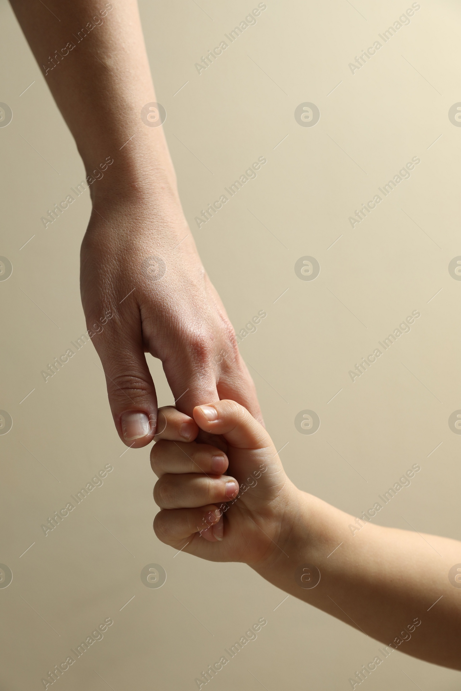 Photo of Mother and child holding hands on beige background, closeup