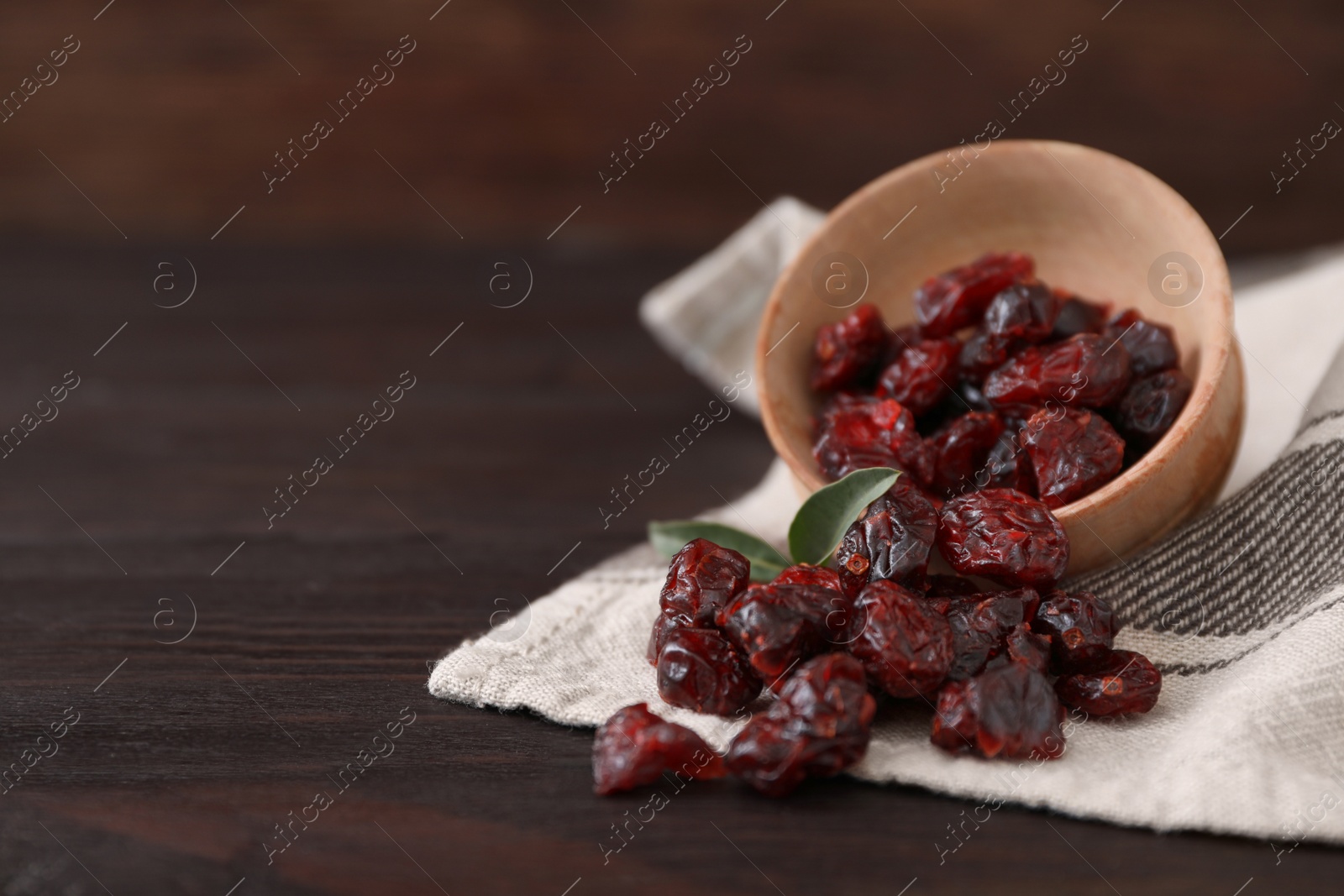Photo of Dried cranberries with bowl on wooden table, closeup. Space for text