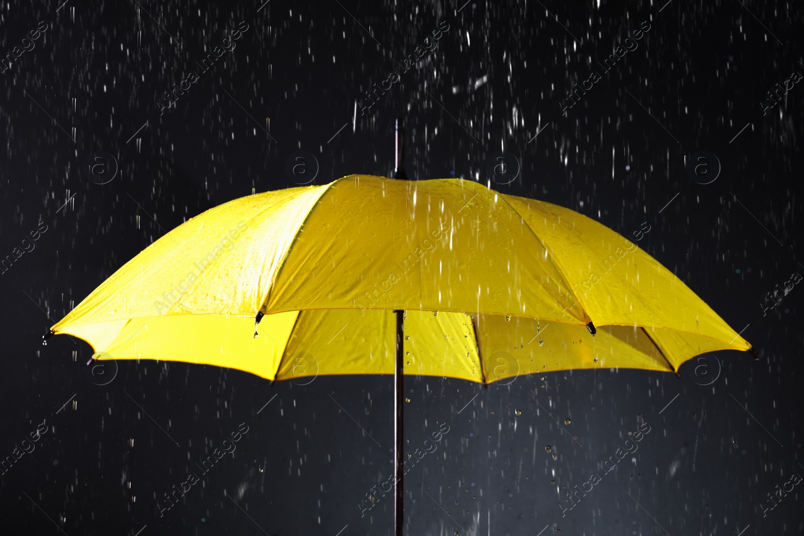 Photo of Bright umbrella under rain on dark background