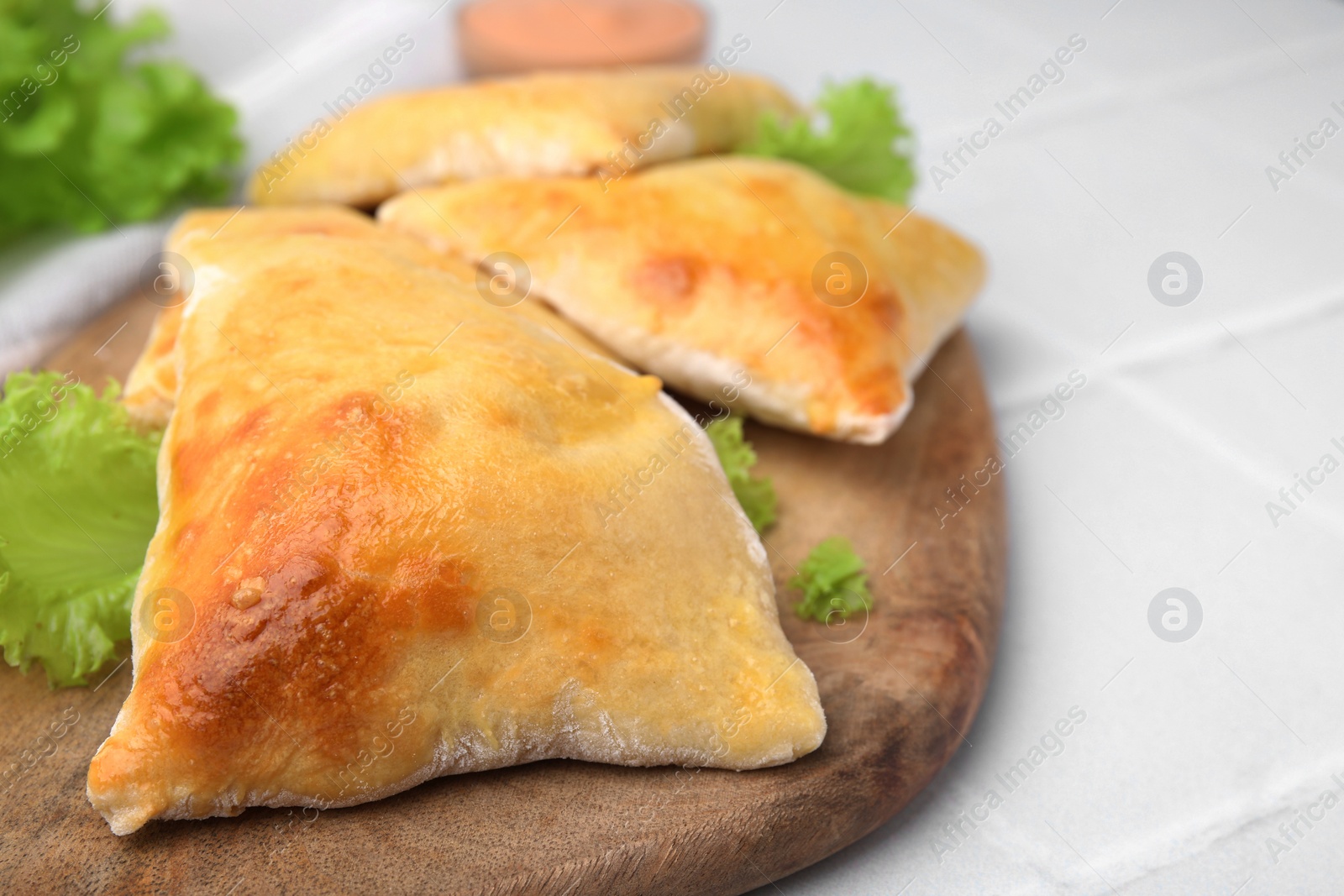 Photo of Delicious samosas and lettuce on white tiled table, closeup. Space for text