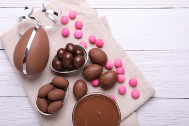 Photo of Delicious chocolate eggs, paste and candies on white wooden table, flat lay