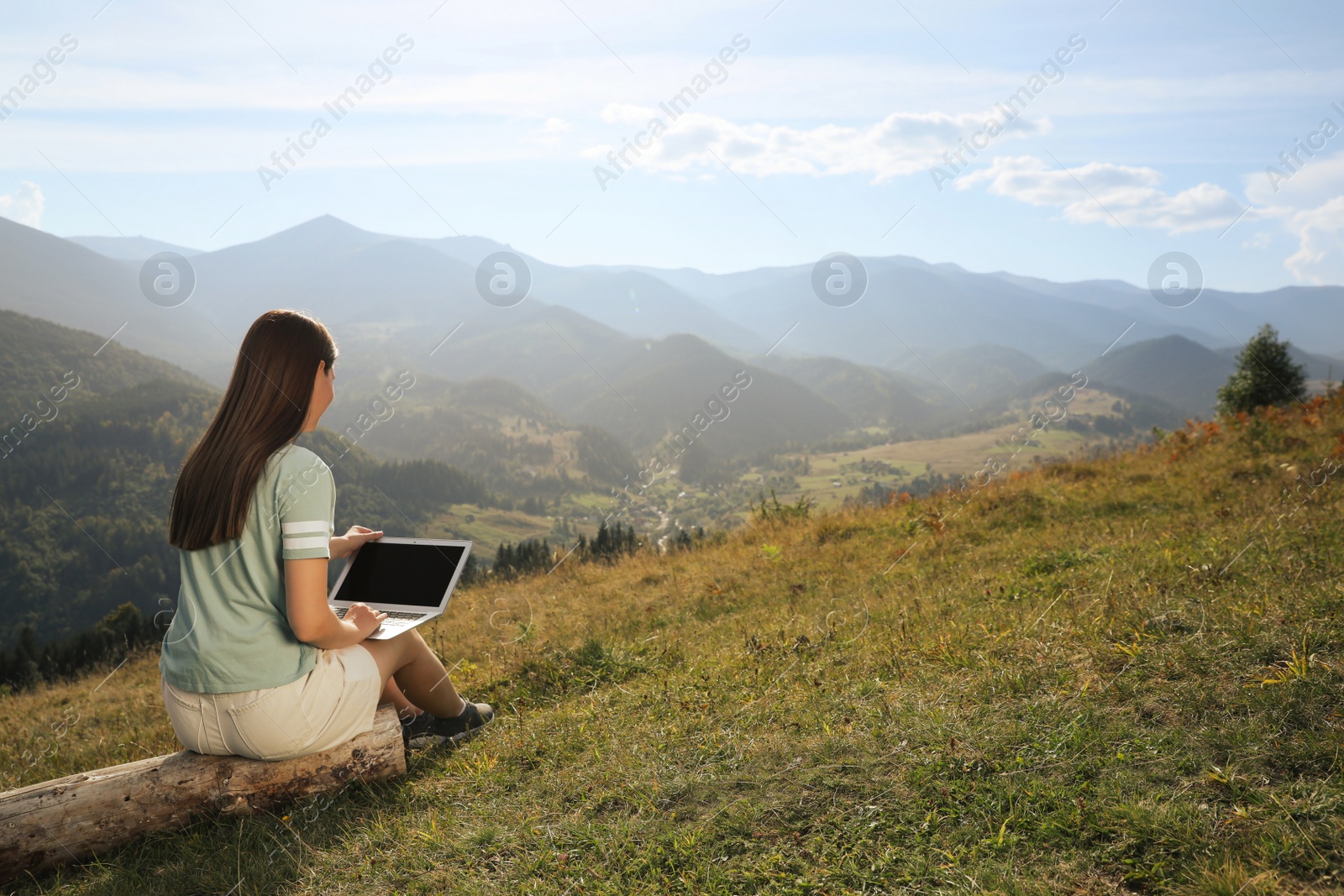 Photo of Young woman working with laptop in mountains on sunny day