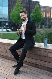 Photo of Smiling businessman eating lunch during break outdoors