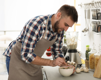 Young man cooking tasty cream soup with mushrooms in kitchen