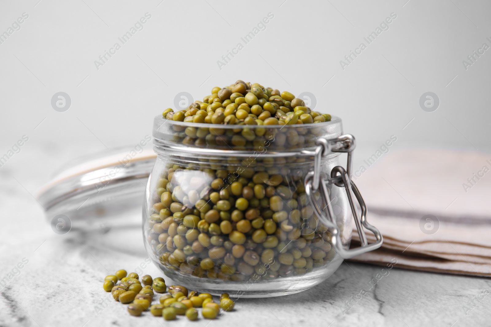 Photo of Glass jar with green mung beans on white textured table, closeup