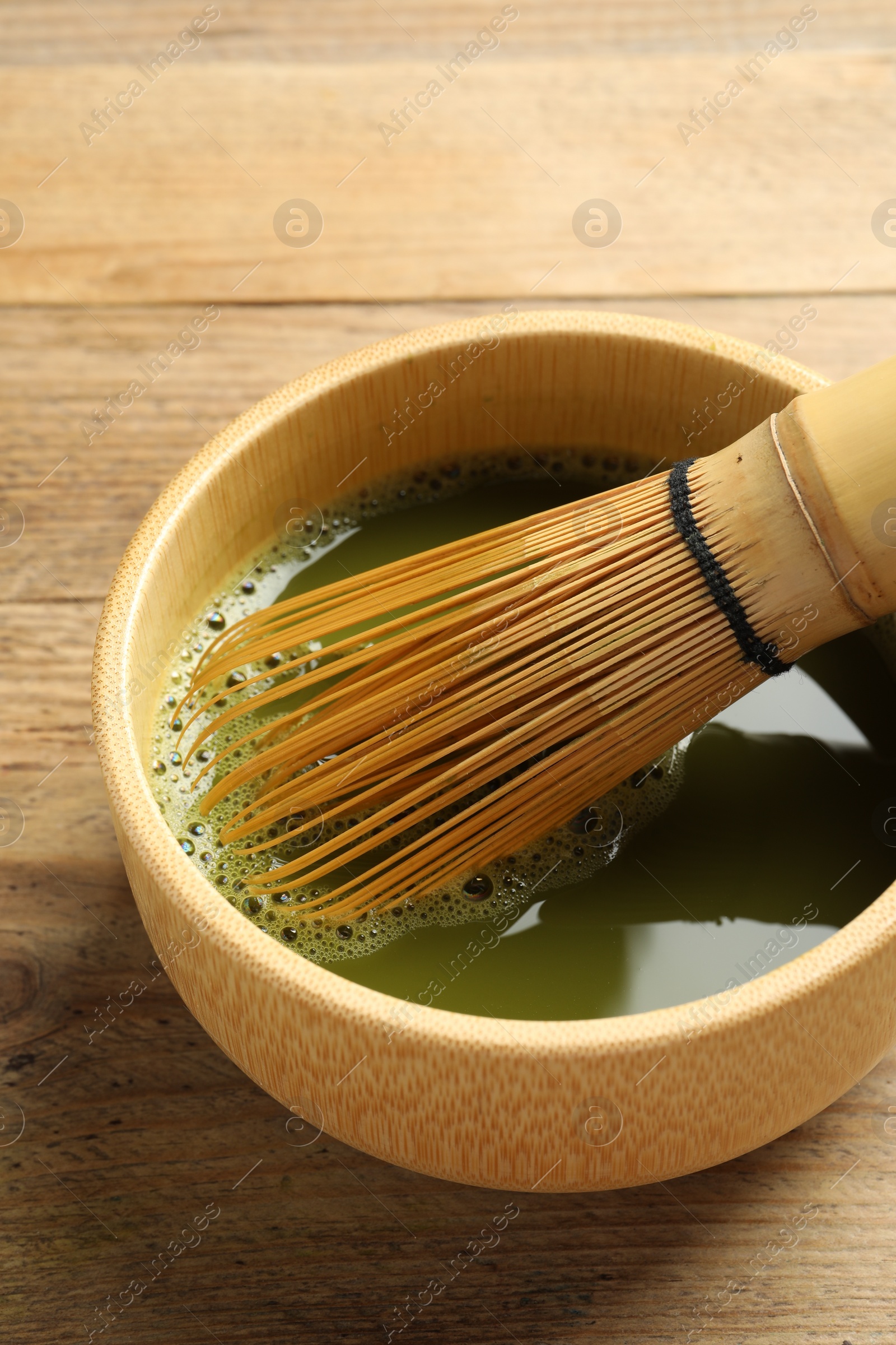 Photo of Cup of fresh matcha tea with bamboo whisk on wooden table, closeup