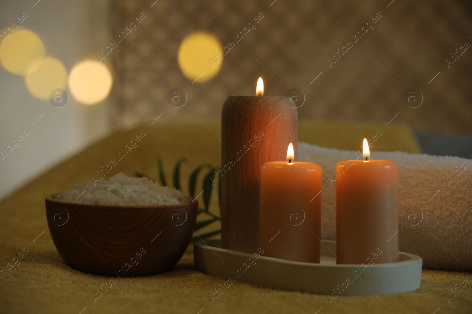 Photo of Spa composition. Burning candles, sea salt and towel on soft yellow surface