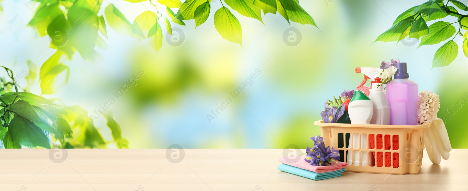 Image of Plastic basket with different detergents on wooden table, space for text. Spring cleaning concept 