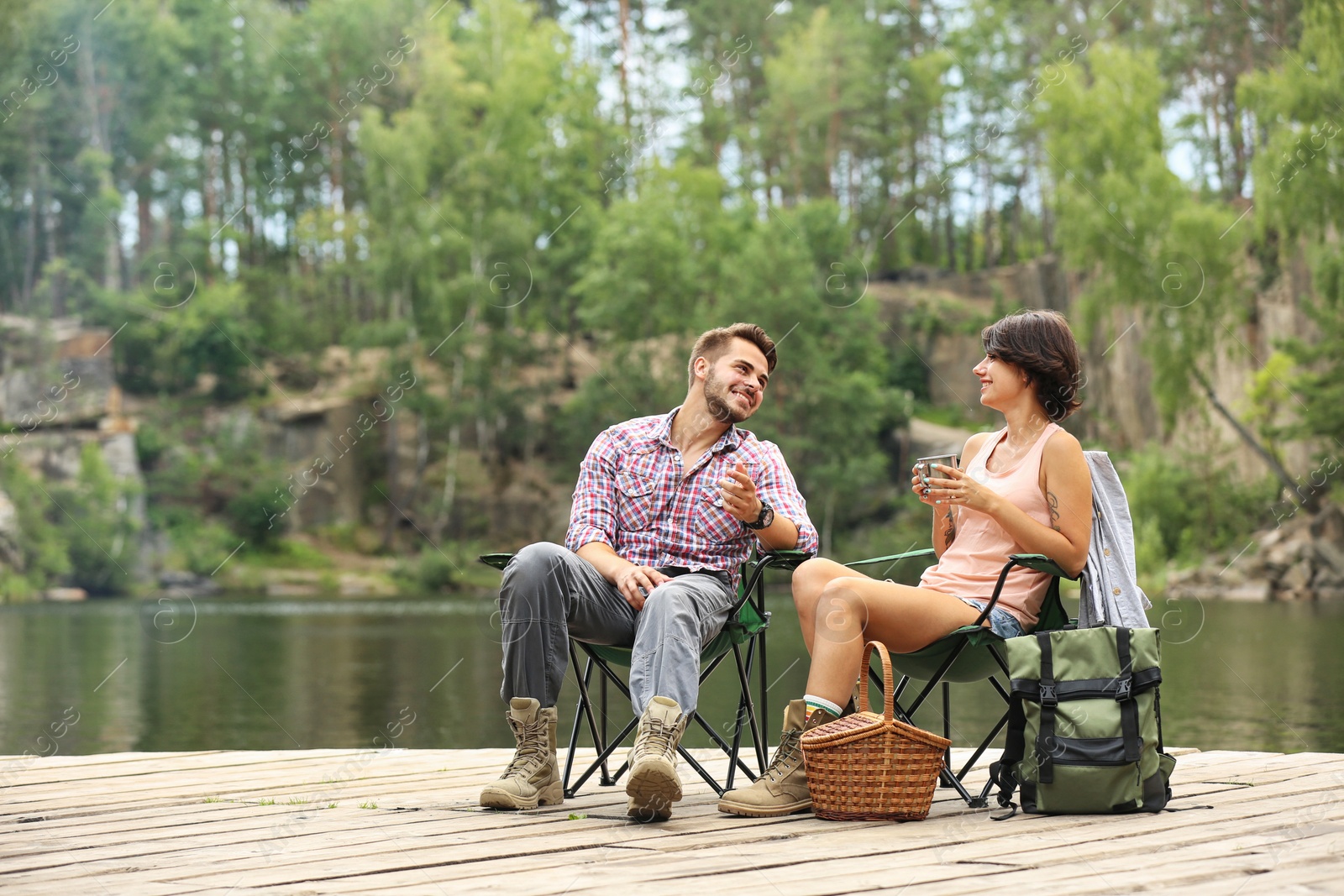 Photo of Young couple resting on pier near lake. Camping season