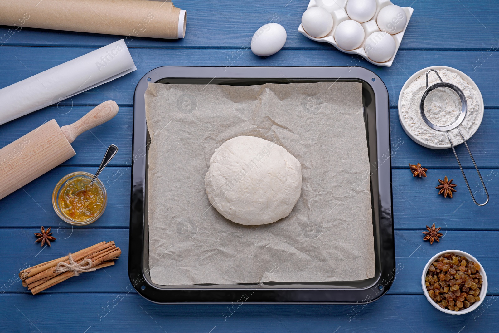 Photo of Baking pan with dough, parchment paper and ingredients on blue wooden table, flat lay