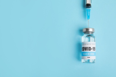 Photo of Filling syringe with coronavirus vaccine on light blue  background, flat lay. Space for text