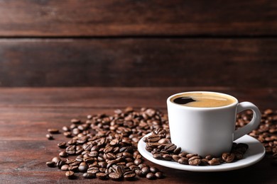 Photo of Cup of hot aromatic coffee and roasted beans on wooden table. Space for text