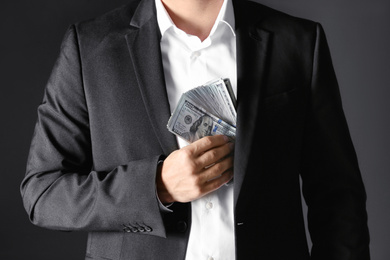 Photo of Man putting bribe money into pocket on black background, closeup