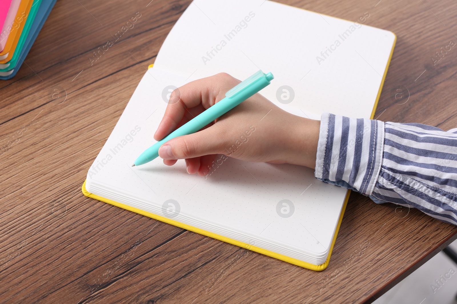 Photo of Woman writing in notebook at wooden table, closeup