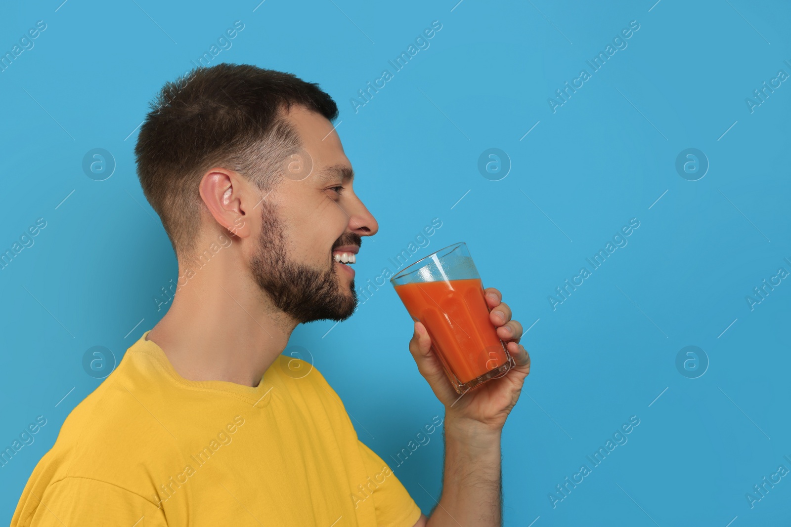 Photo of Man drinking delicious juice on light blue background, space for text