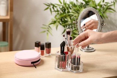 Photo of Woman taking cosmetic products for makeup from organizer on dressing table, closeup. Space for text