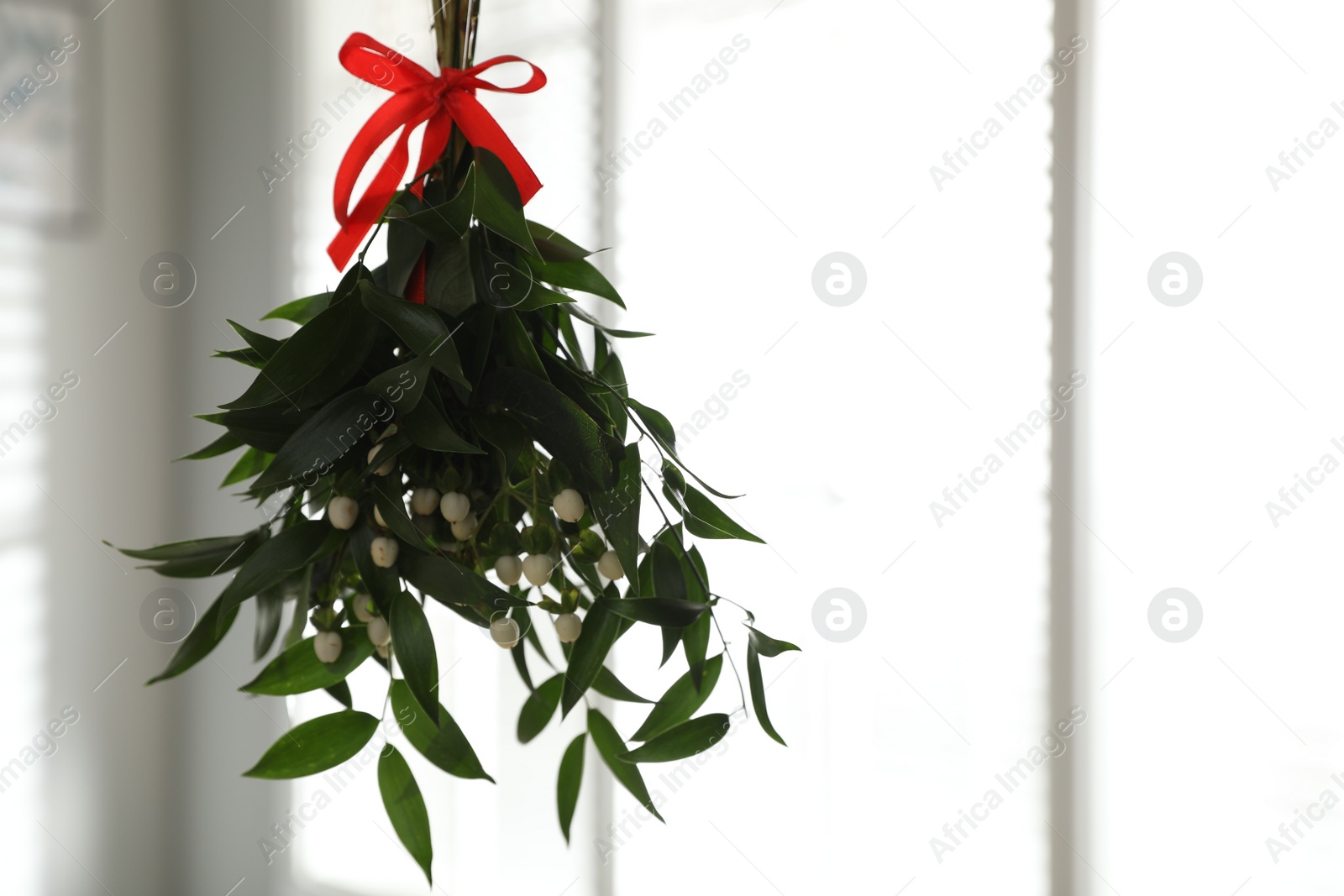 Photo of Mistletoe bunch with red bow hanging indoors, space for text. Traditional Christmas decor