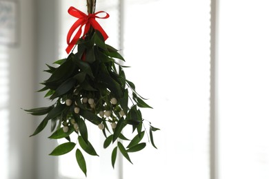 Photo of Mistletoe bunch with red bow hanging indoors, space for text. Traditional Christmas decor