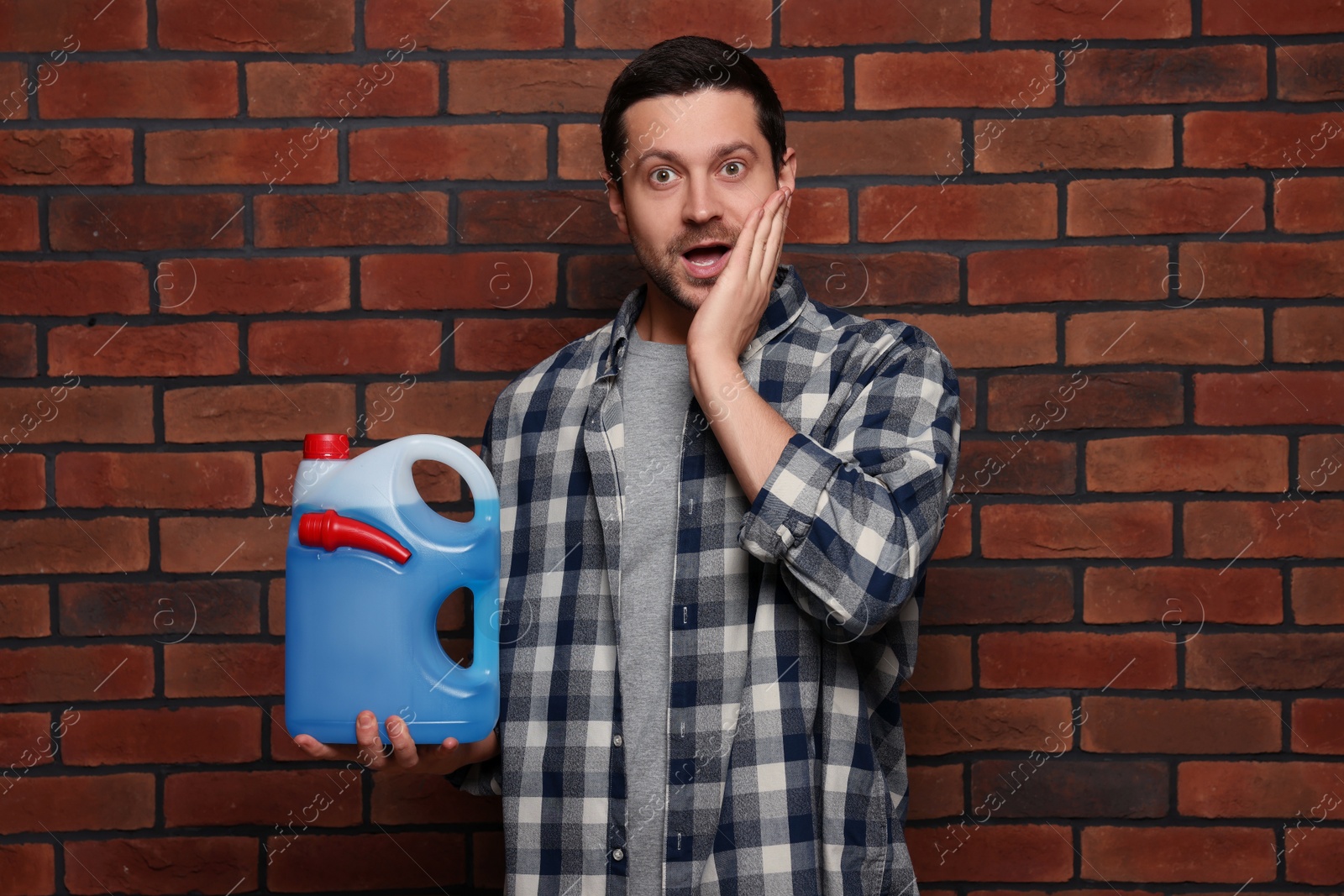 Photo of Emotional man holding canister with blue liquid near brick wall