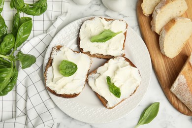 Photo of Bread with cream cheese and basil on white marble table, flat lay