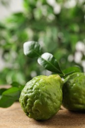 Photo of Fresh ripe bergamot fruits with green leaves on wooden table against blurred background, closeup. Space for text