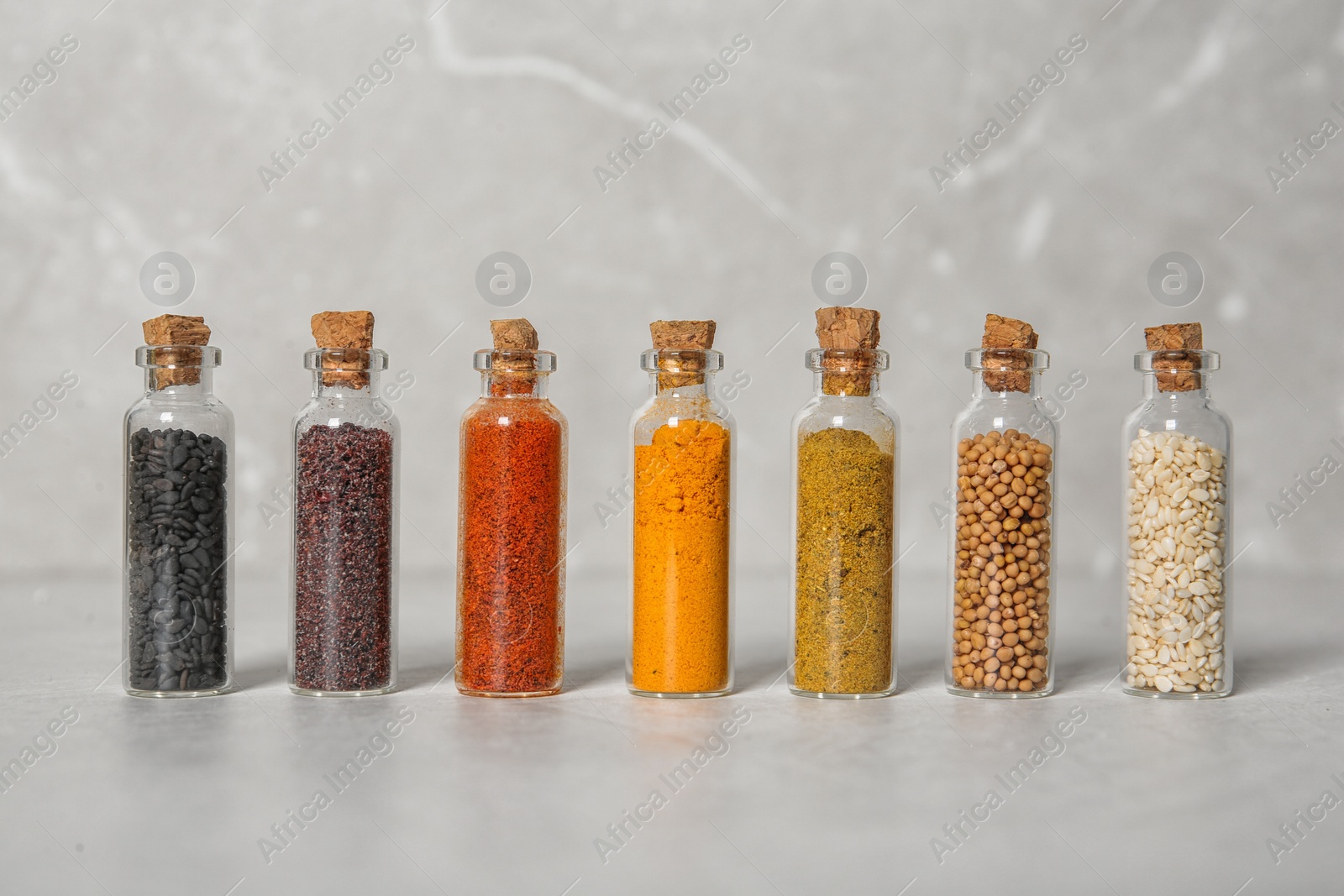 Photo of Row of small glass bottles with different spices on color background
