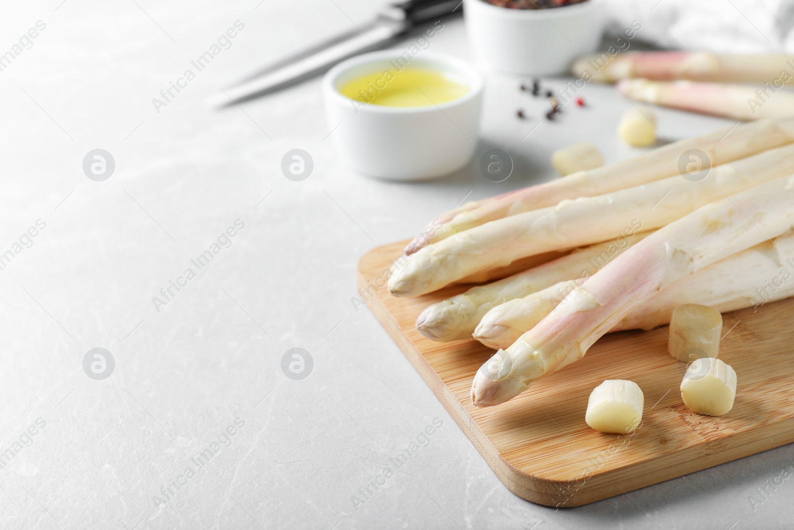 Photo of Fresh white asparagus and wooden board on grey marble table, closeup. Space for text