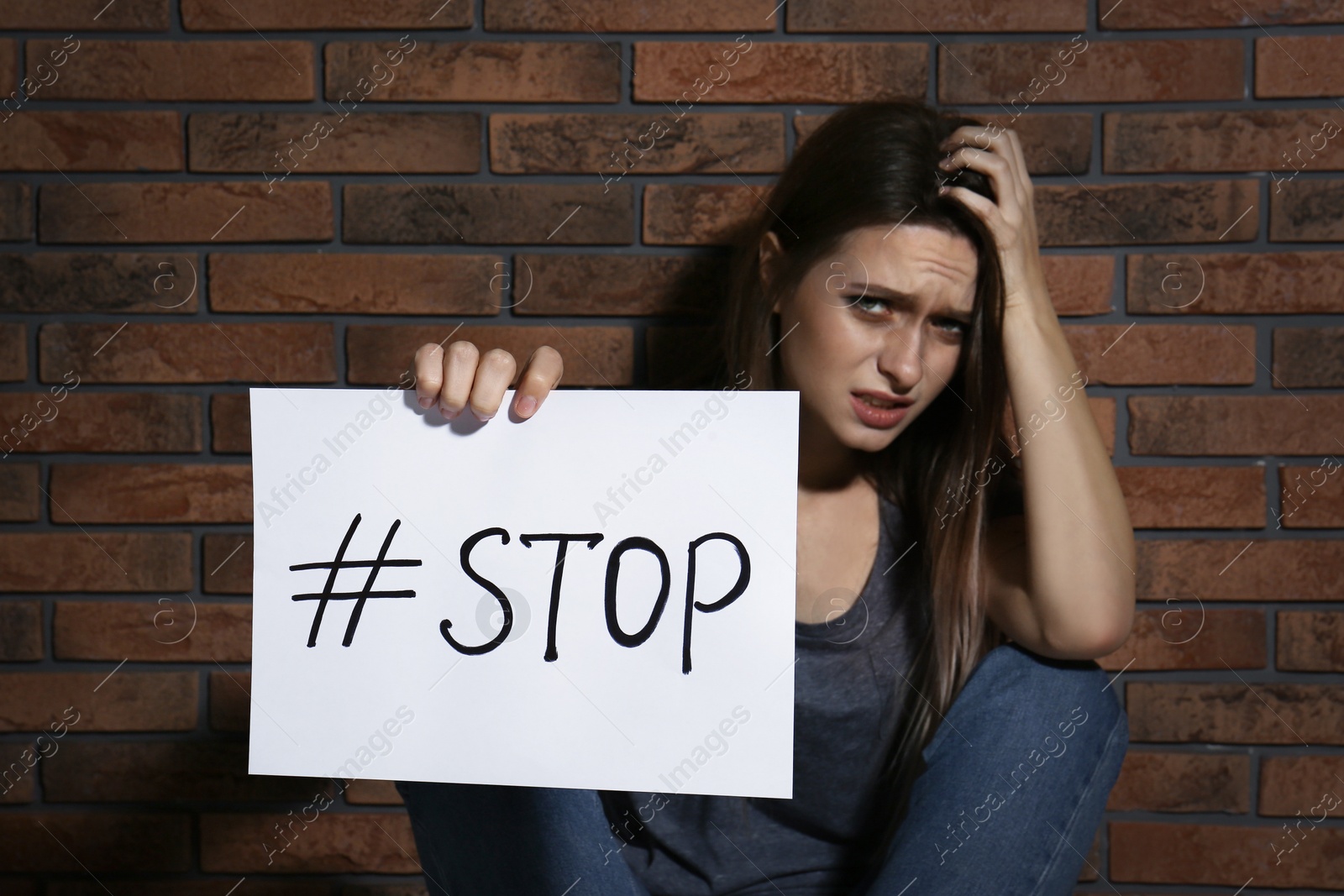 Photo of Crying young woman with hashtag STOP near brick wall. Domestic violence concept