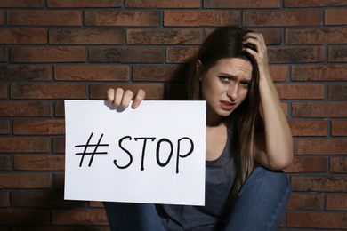 Crying young woman with hashtag STOP near brick wall. Domestic violence concept