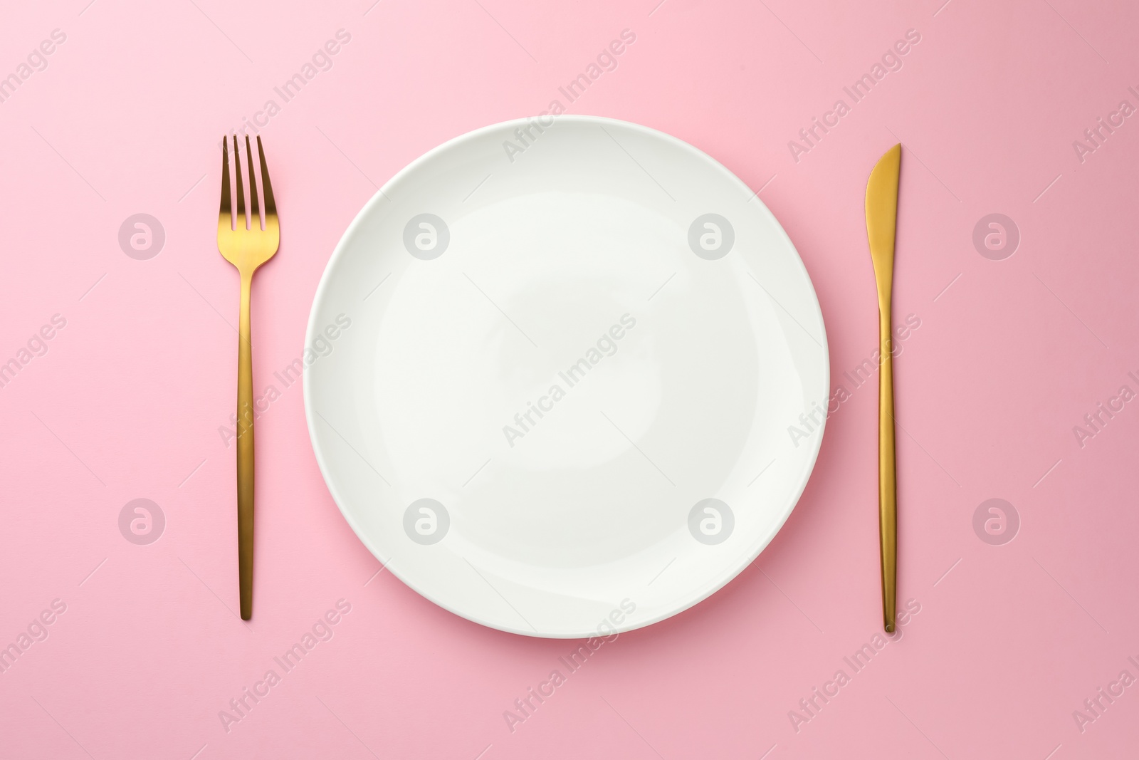 Photo of Empty plate, fork and knife on pink background, top view