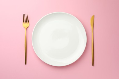 Empty plate, fork and knife on pink background, top view