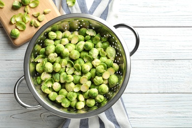 Photo of Colander with Brussels sprouts and napkin on wooden background, top view. Space for text