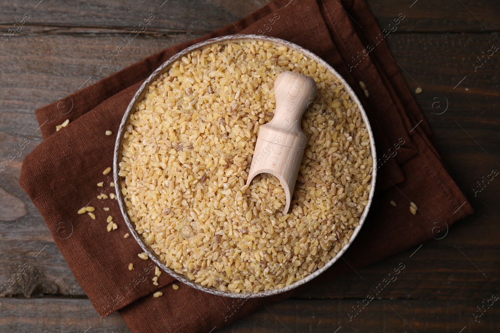 Photo of Bowl and scoop with raw bulgur on wooden table, top view