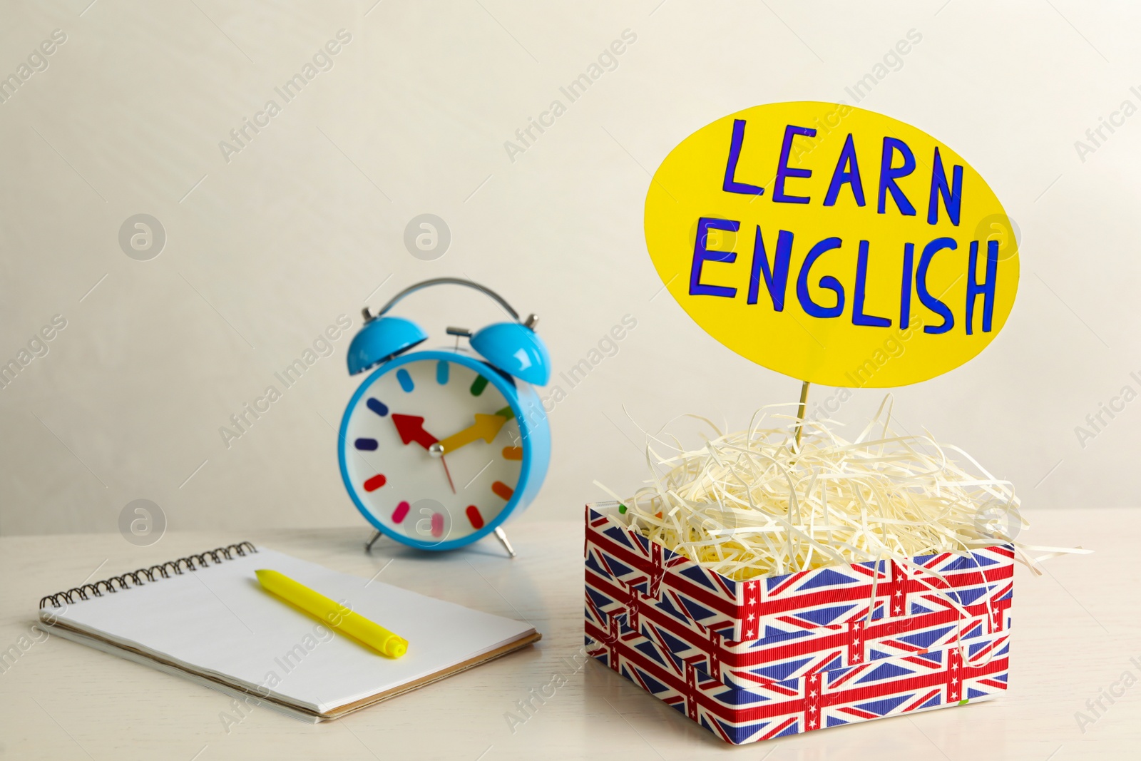 Photo of Notepad, alarm clock and sign with phrase Learn English in box on white wooden table