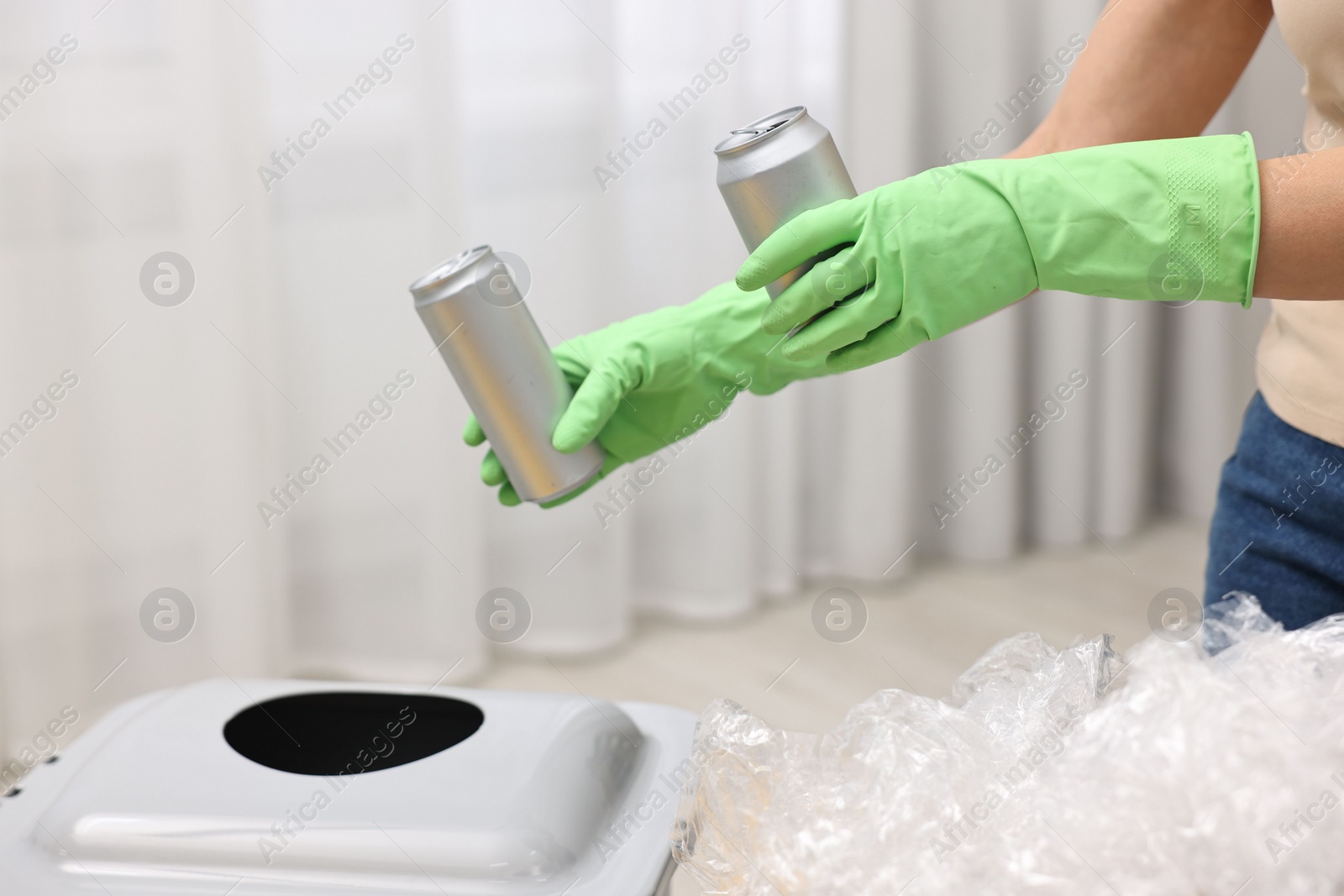 Photo of Garbage sorting. Woman throwing metal cans into trash bin in room, closeup