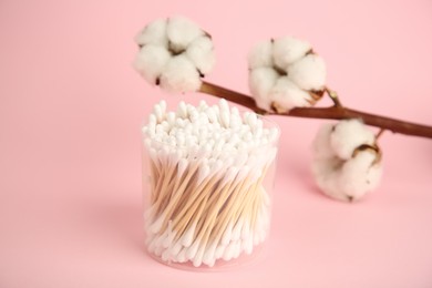 Photo of Container with cotton buds and flowers on pink background