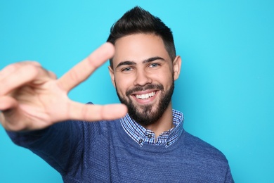 Photo of Happy young man showing victory gesture on color background