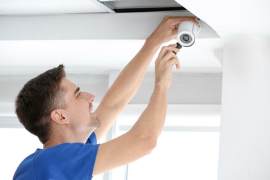 Technician installing CCTV camera on ceiling indoors