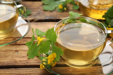 Photo of Glass cup of aromatic celandine tea and flowers on wooden table, closeup