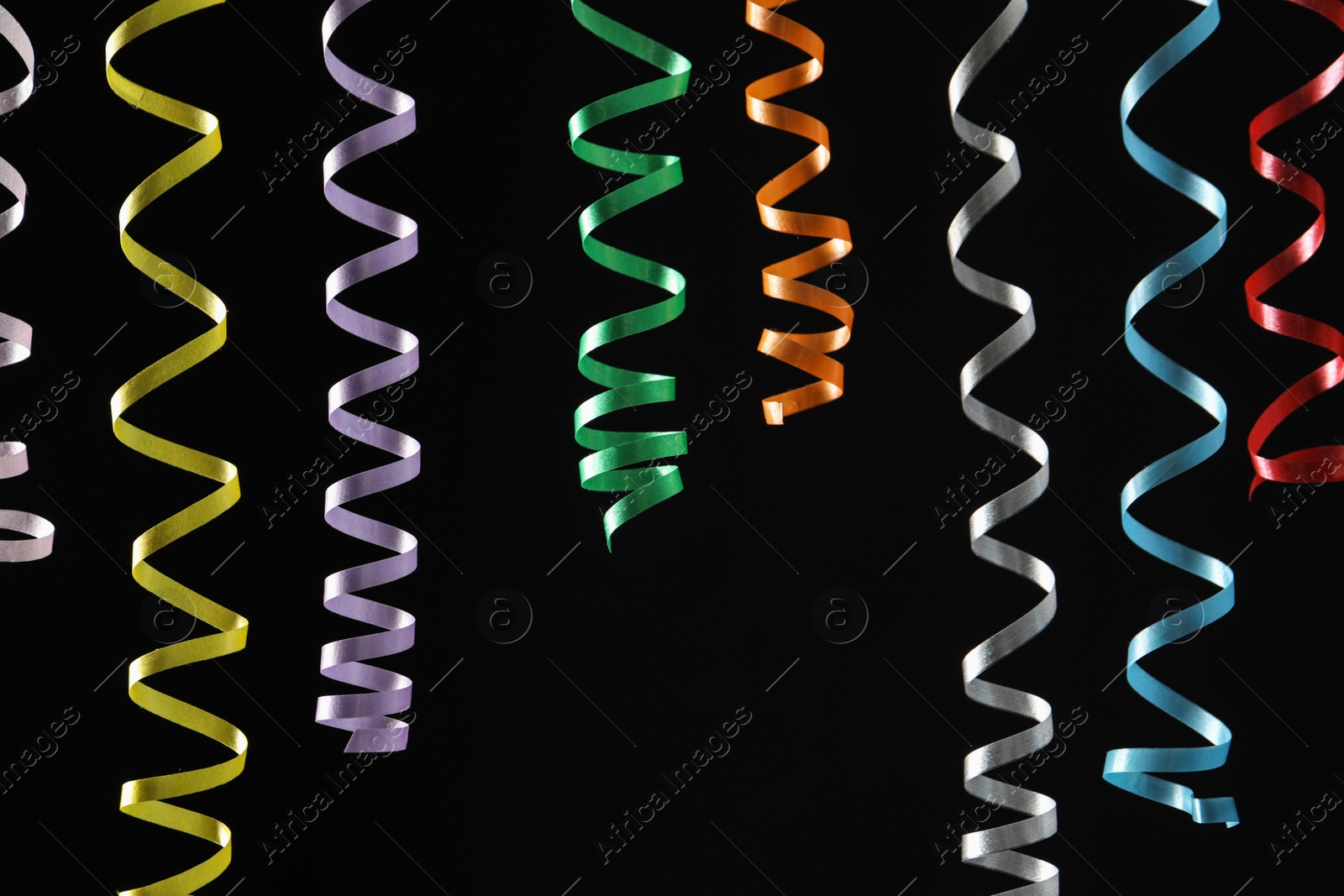 Photo of Many colorful serpentine streamers on black background