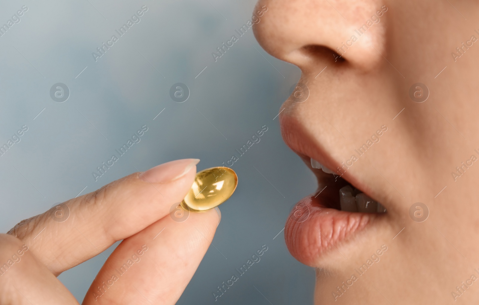 Photo of Woman taking fish oil pill on color background, closeup