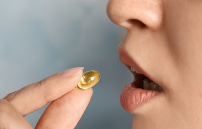 Woman taking fish oil pill on color background, closeup