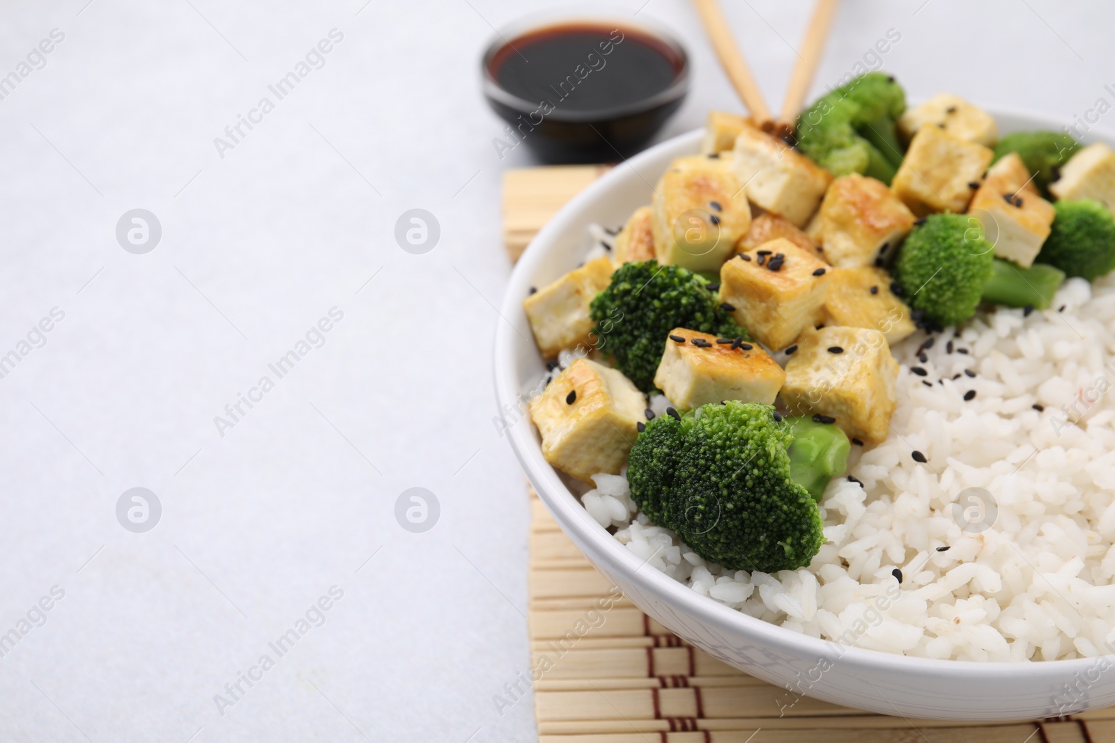 Photo of Bowl of rice with fried tofu and broccoli on white table, closeup. Space for text