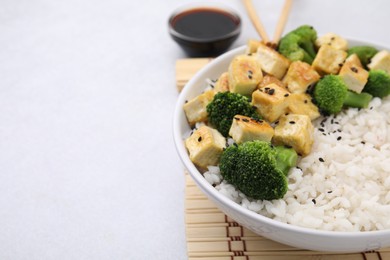 Bowl of rice with fried tofu and broccoli on white table, closeup. Space for text