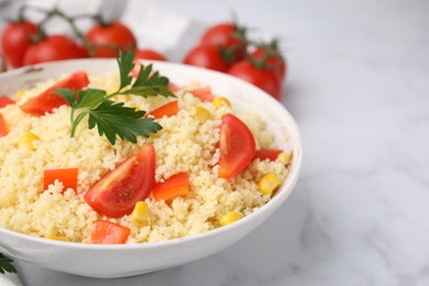 Photo of Tasty couscous with parsley, corn and tomatoes in bowl on white marble table, closeup. Space for text