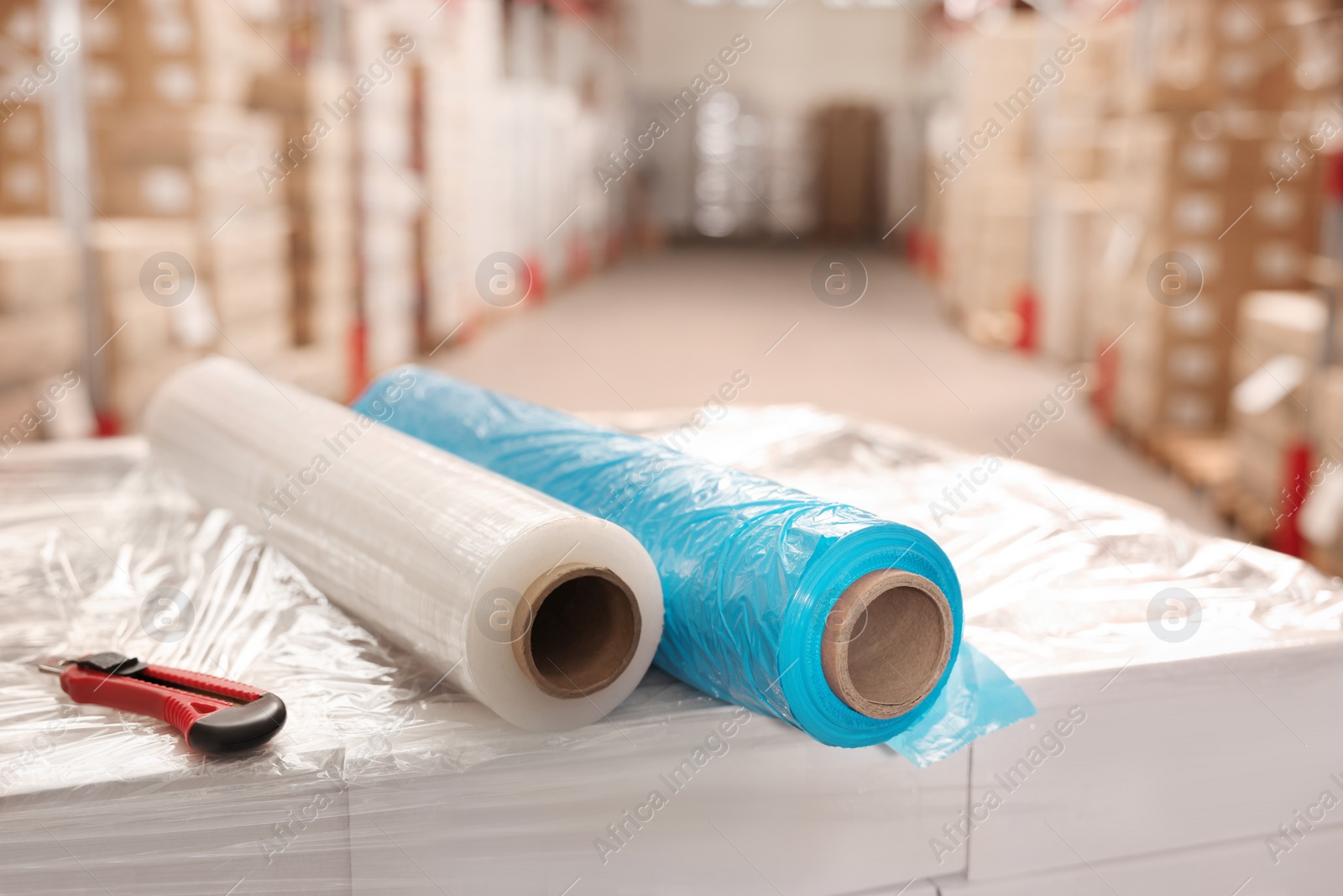 Photo of Rolls of different stretch wraps and utility knife on boxes in warehouse